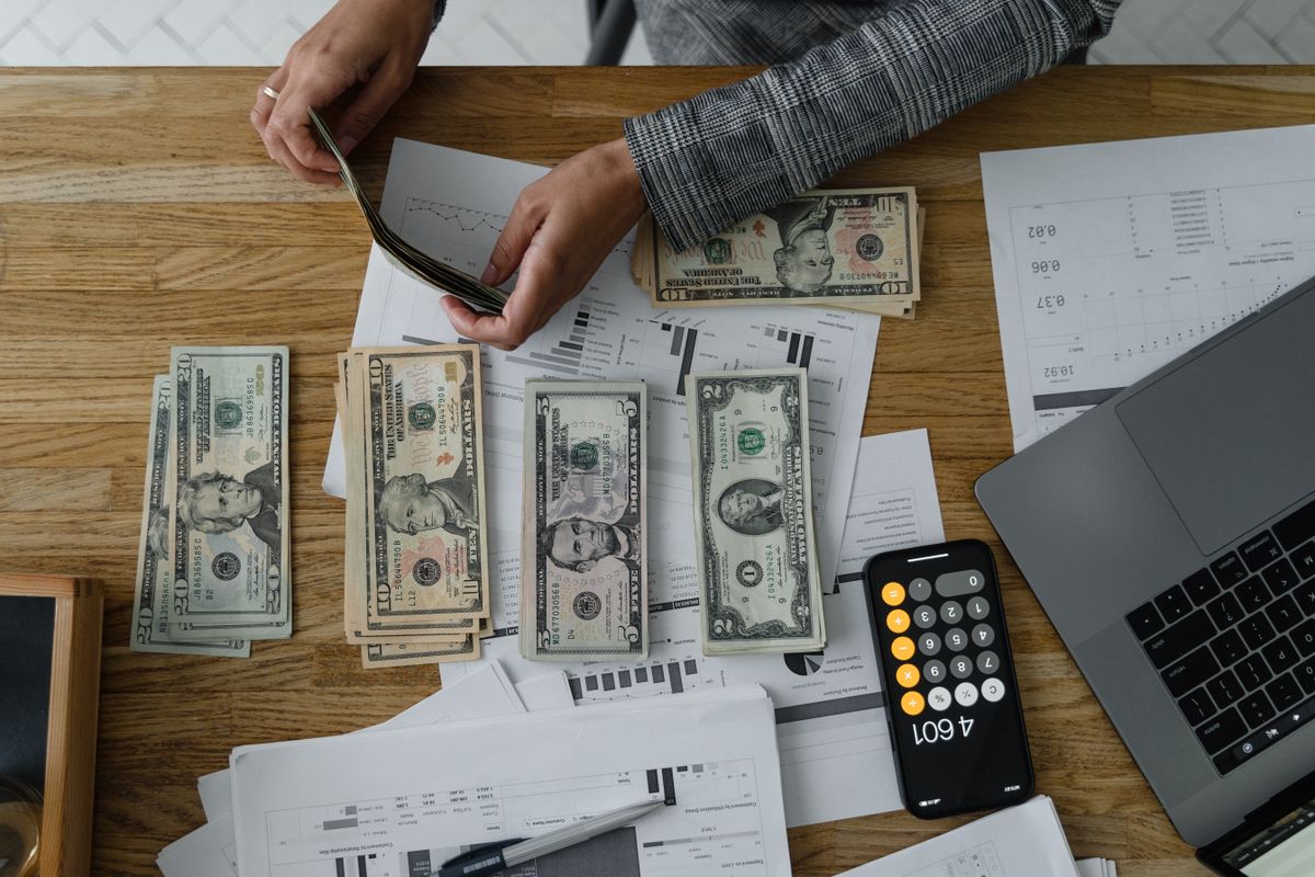 A person using a calculator next to cash and paperwork on a desk